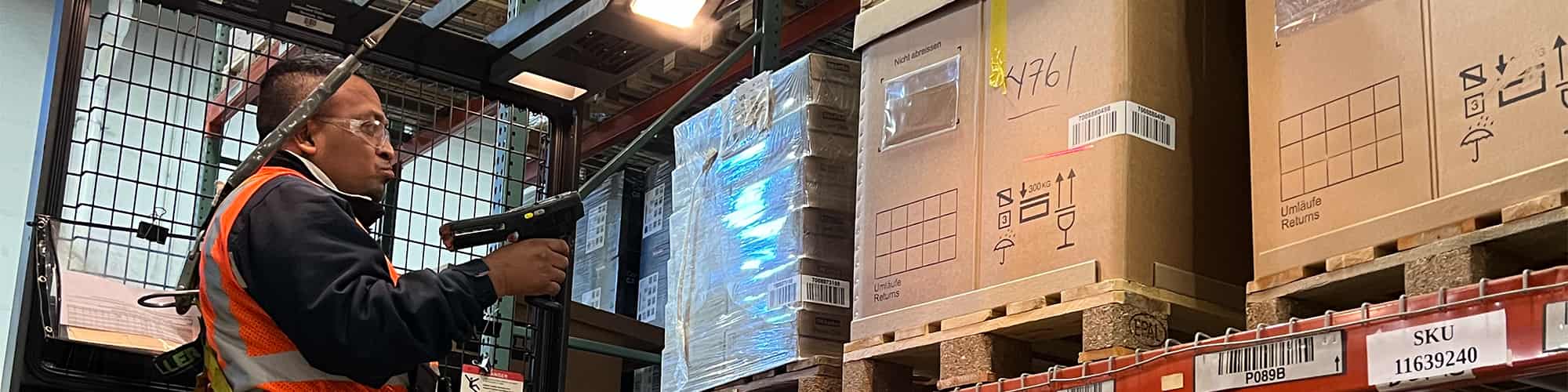 worker scanning barcodes on boxed pallets in warehouse storage racks